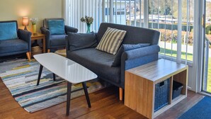 A modern living room with a sofa, chairs, a coffee table, and a view through large windows.