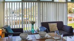 A dining area with a table set for four, a sofa, and a view through large windows.