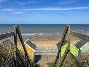 Un escalier en bois mène à des cabanes de plage offrant une vue sur la mer.