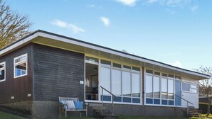 A modern single-story house with a large sliding glass door entrance, a small porch with a bench, and a clear sky.