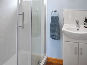 Une salle de bain avec une douche à parois de verre, un lavabo muni d’un distributeur de savon et une serviette suspendue à un anneau métallique.