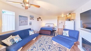 A compact room with a bed, two sofas, a ceiling fan, a TV, and a small kitchen area. - NEW! Walk to town and beach, Balcony, Romantic, (Sandpiper Approach) (Long Beach)