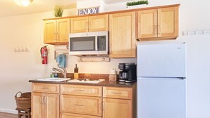 A kitchen with wooden cabinets, a microwave, a coffee maker, and a refrigerator. - NEW! Walk to town and beach, Balcony, Romantic, (Sandpiper Approach) (Long Beach)
