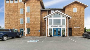 A two-story building with a sign reading "BOLSTAD WEST" at the entrance. There are two vehicles parked in front, and a handicapped parking sign is visible. - NEW! Walk to town and beach, Balcony, Romantic, (Sandpiper Approach) (Long Beach)