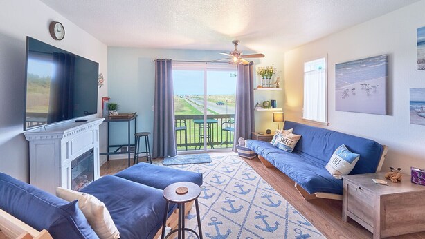 A cozy living room with a TV, sofa, and a balcony with a view. - NEW! Walk to town and beach, Balcony, Romantic, (Sandpiper Approach) (Long Beach)
