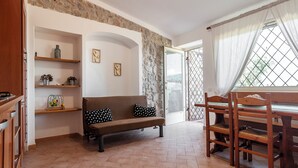 Un'accogliente zona giorno con un divano marrone, scaffali in legno, un tavolo da pranzo con sedie e una vista attraverso una finestra con tende.