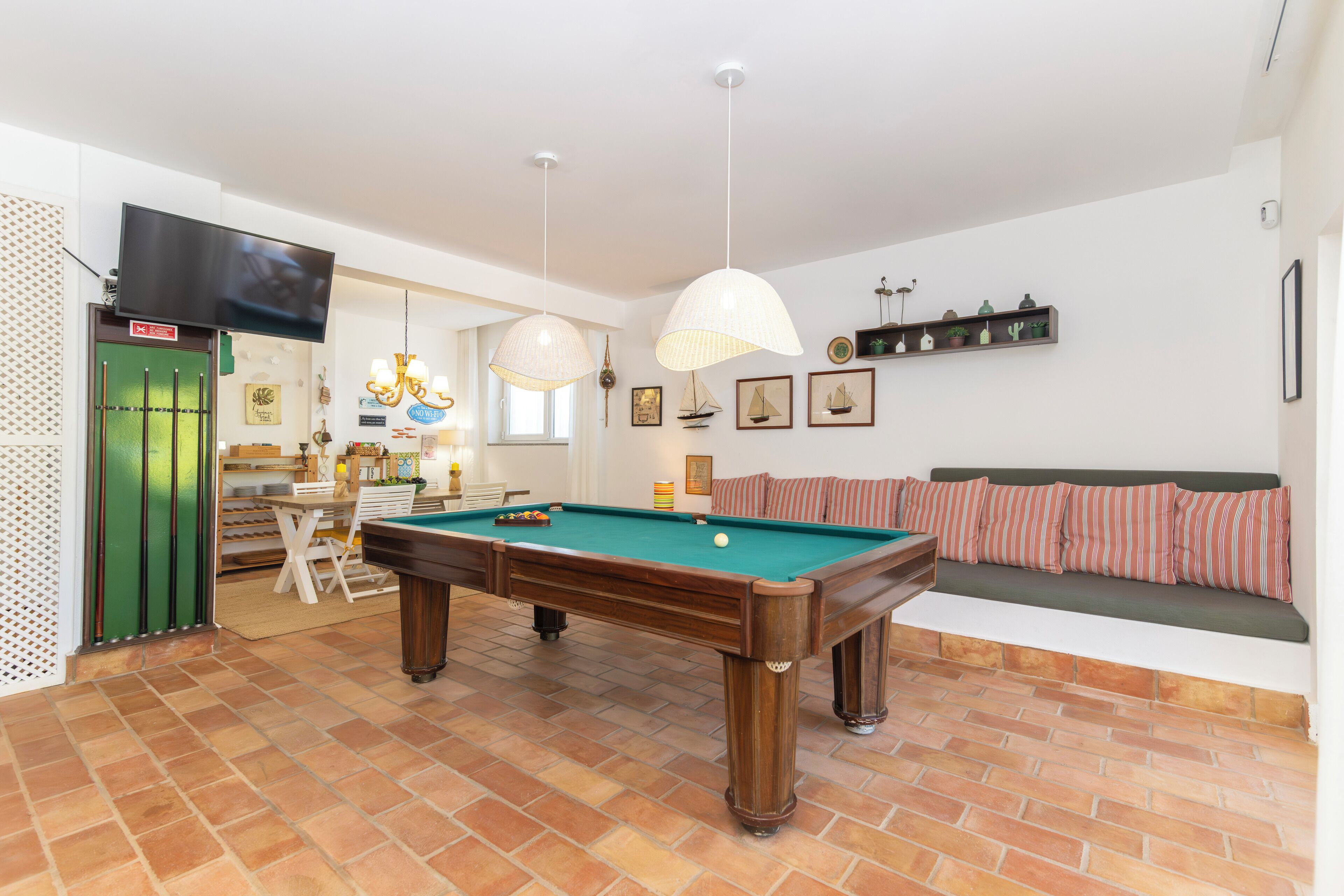 Une table de billard dans une pièce où se trouvent un canapé vert, un téléviseur fixé au mur et une étagère ornée d’objets décoratifs.