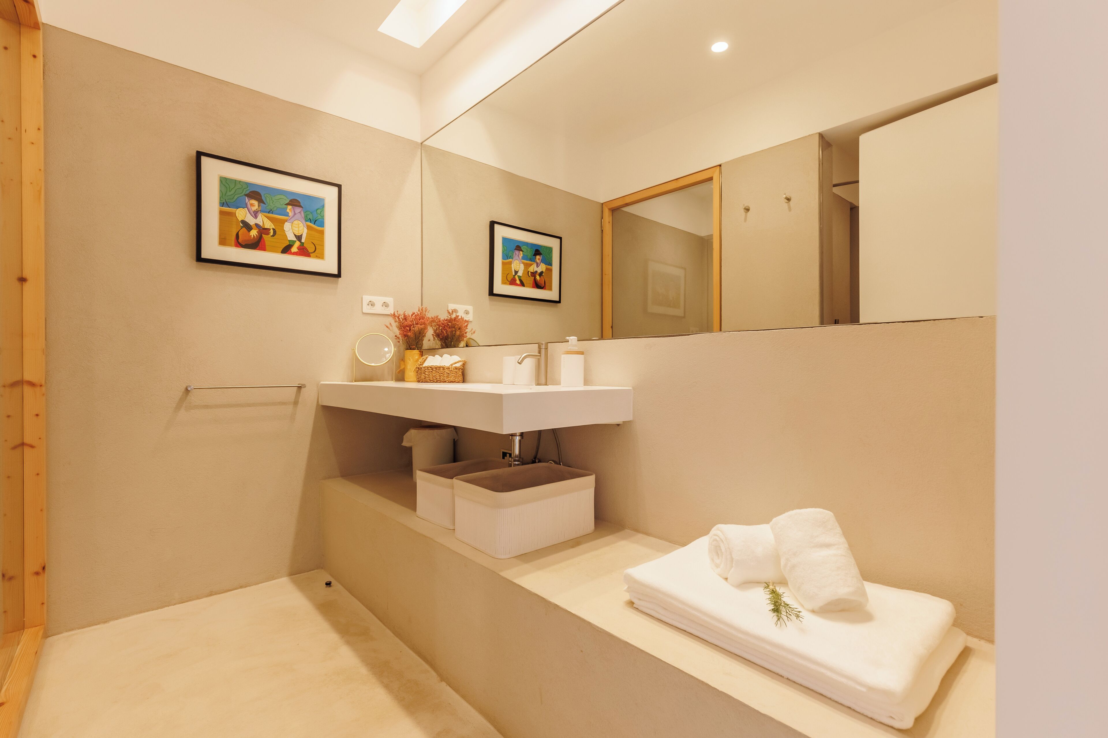 A modern bathroom with a large mirror, two framed artworks, a white sink, and a neatly folded towel on the counter.