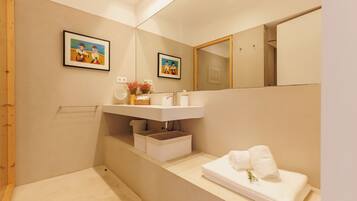 A modern bathroom with a large mirror, two framed artworks, a white sink, and a neatly folded towel on the counter.