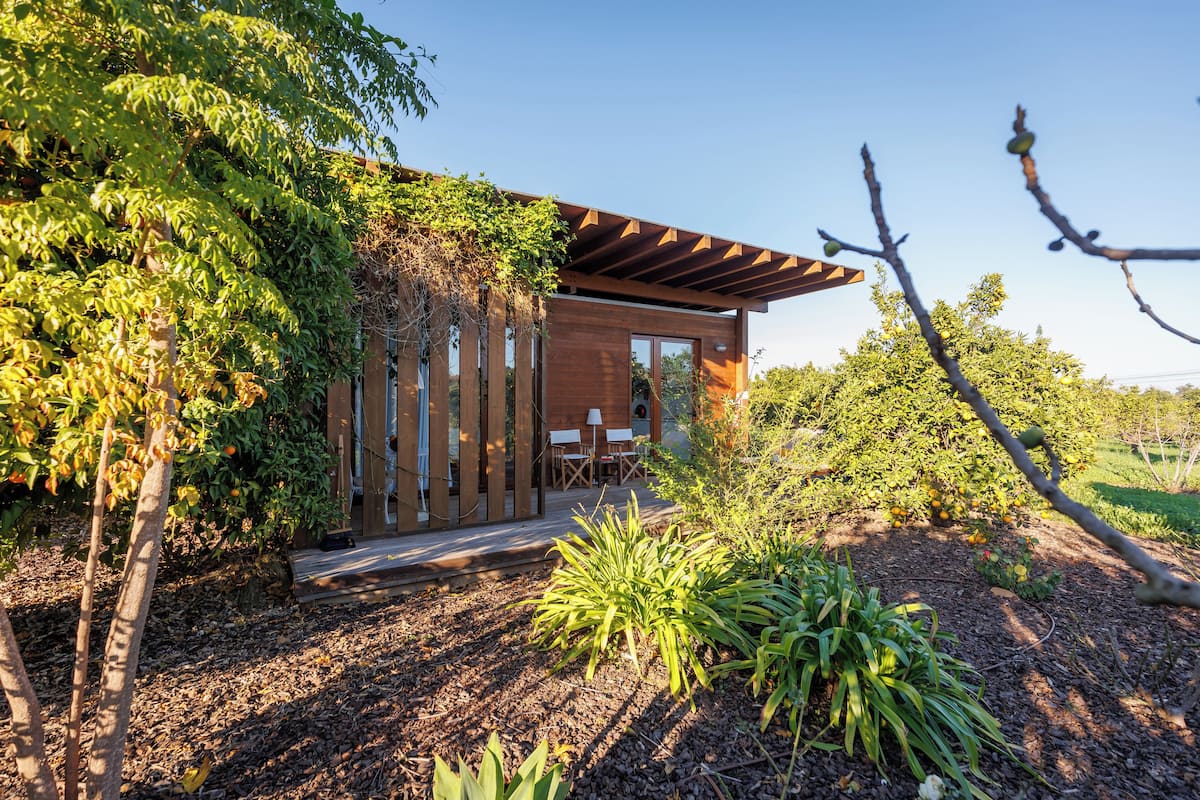 A modern house with a wooden exterior, a patio with outdoor furniture, and a garden with various plants and trees.