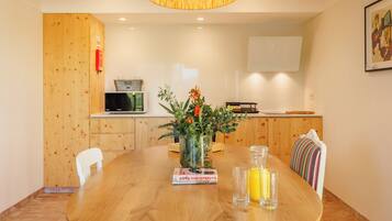A dining area with a wooden table, chairs, a vase with flowers, a book, and a glass bottle.