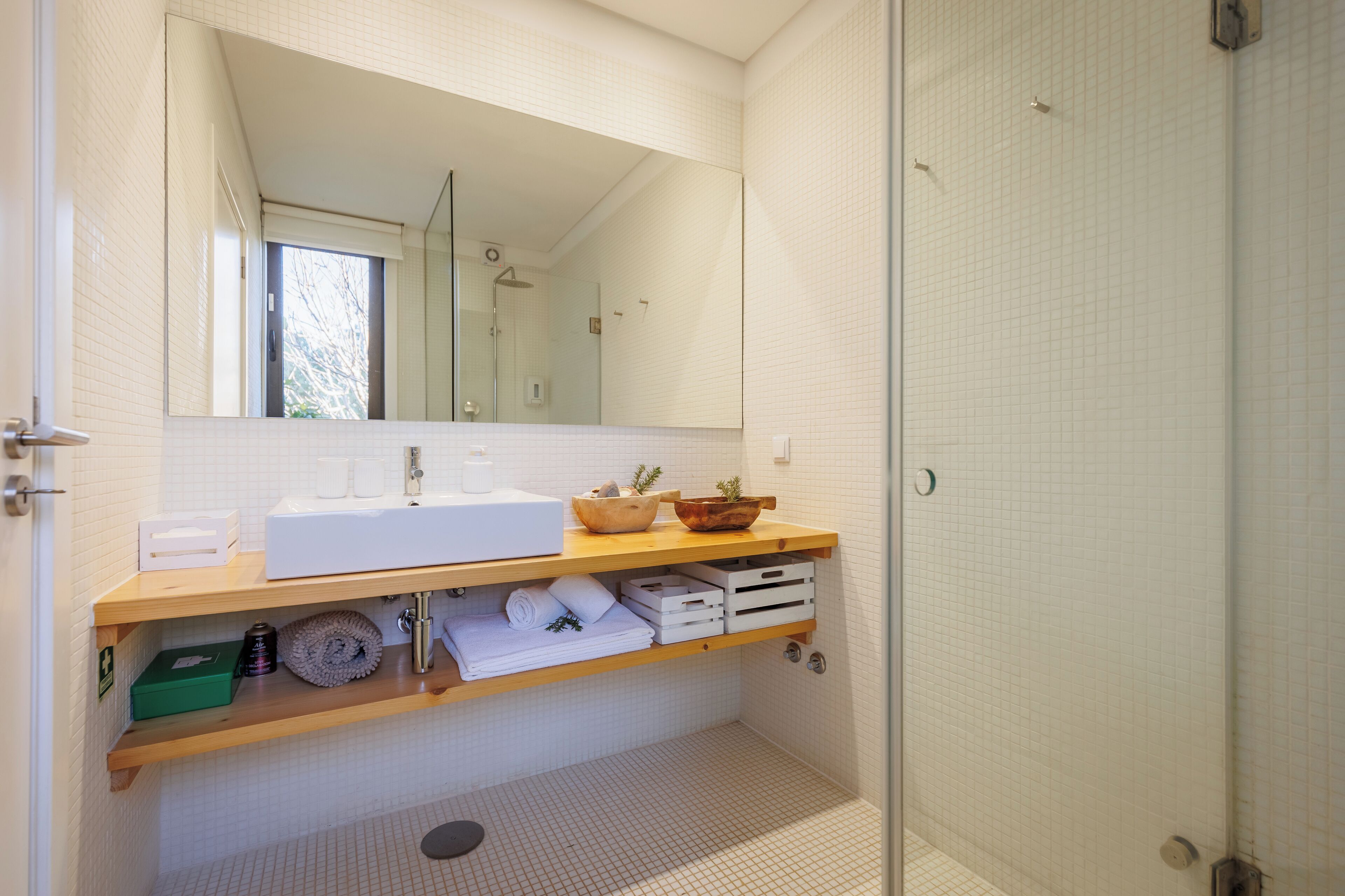 A modern bathroom with a large mirror, white sink, wooden shelves, and a shower area.
