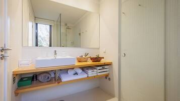A modern bathroom with a large mirror, white sink, wooden shelves, and a shower area.