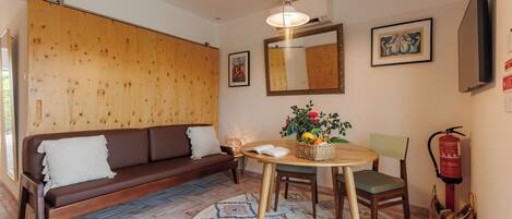 A cozy living room with a brown sofa, a wooden wall, a round table with a basket of fruit, and a fire extinguisher.