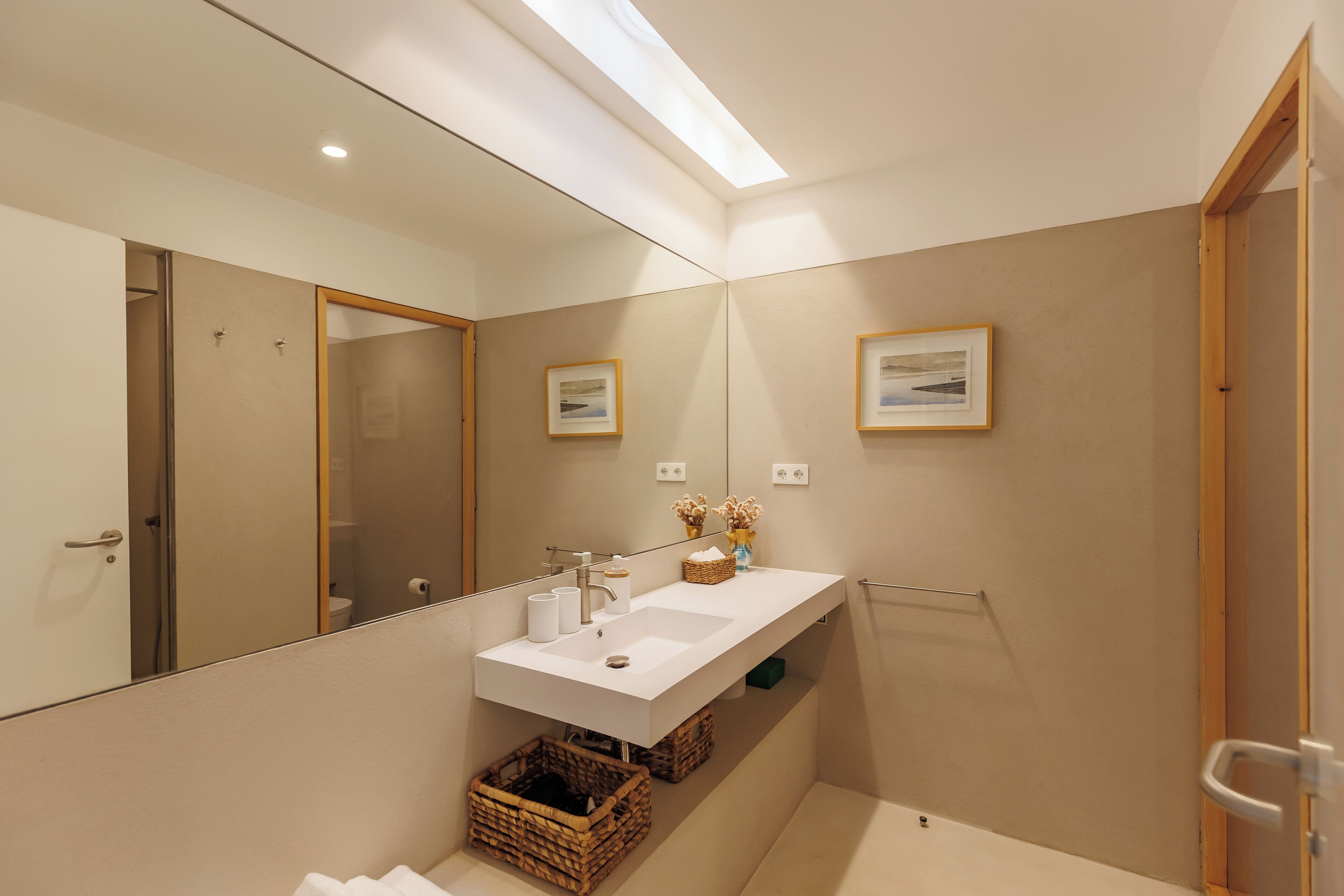 Un baño moderno con un espejo grande, un lavabo blanco y una zona de ducha.