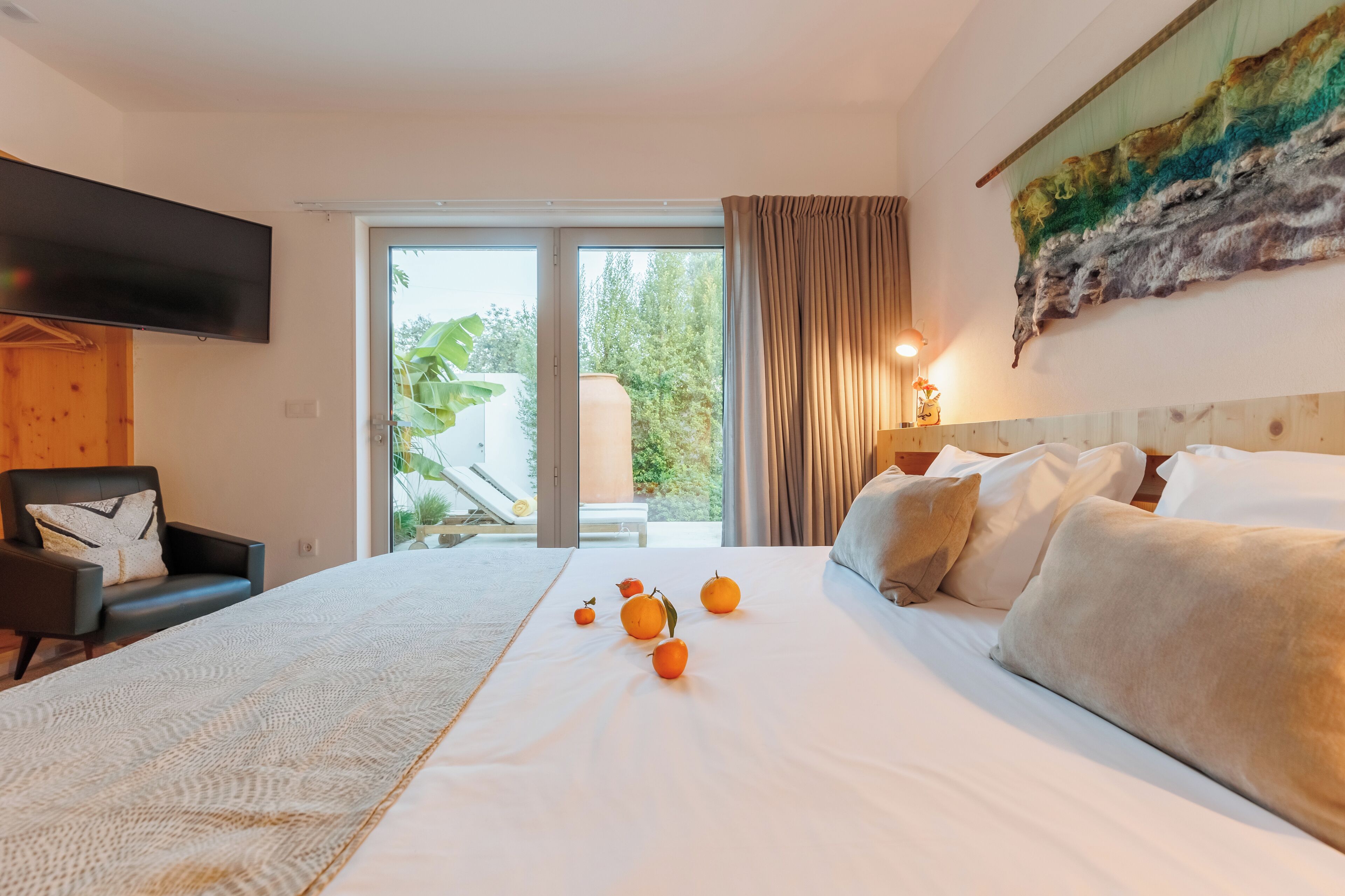 A hotel room with a large bed, a flat-screen TV, a chair, and a view of the outdoors through a sliding glass door.