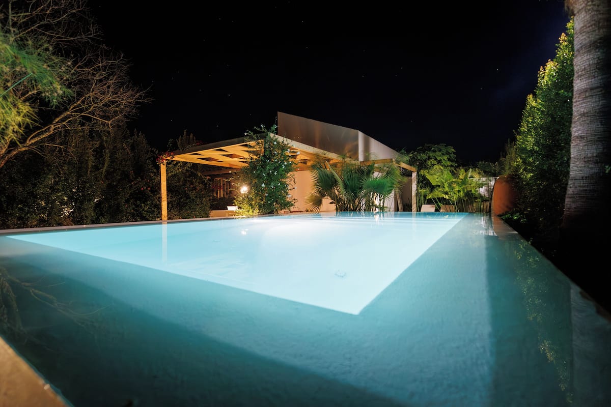 A nighttime swimming pool with a modern structure and surrounding greenery.