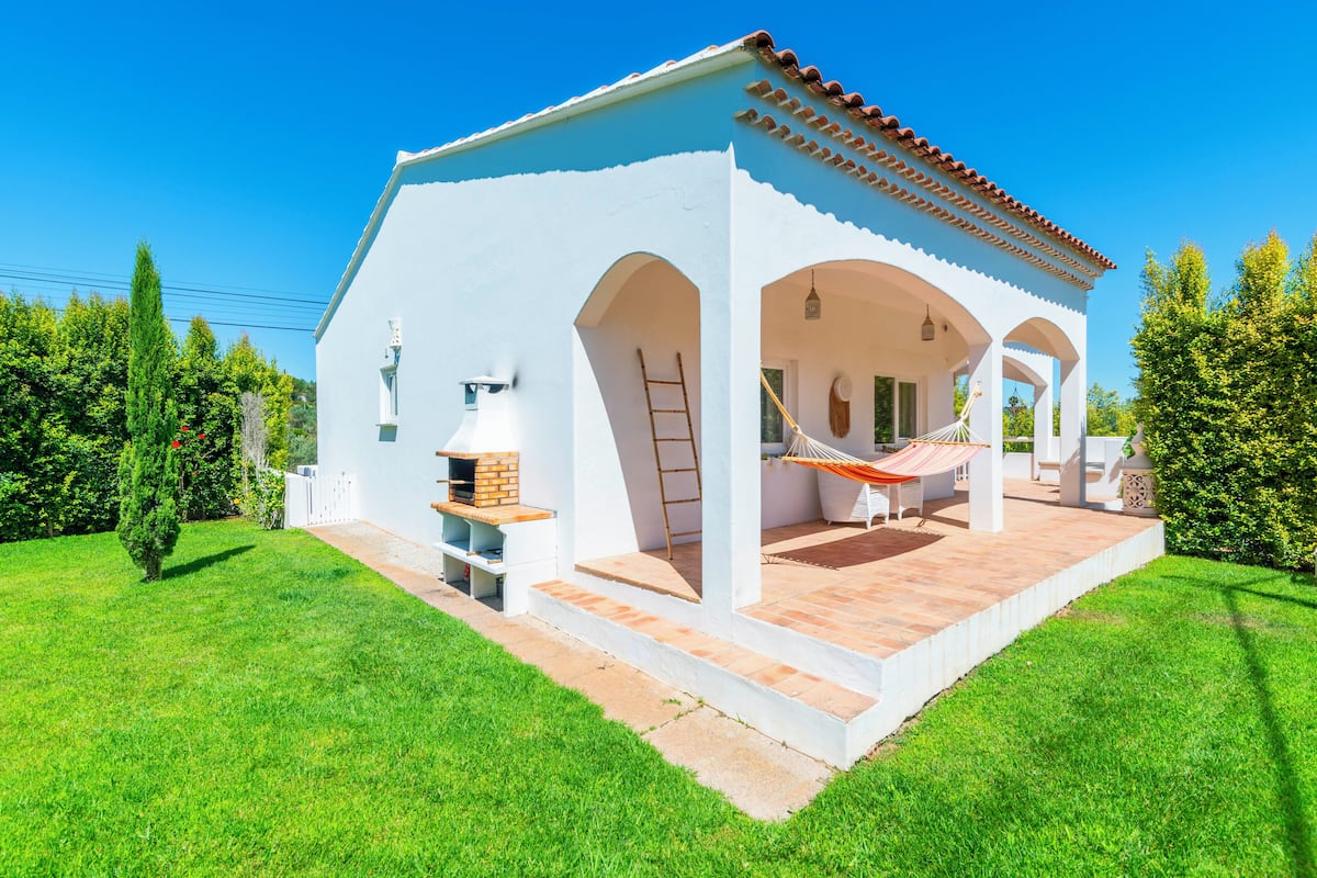 A white building with a tiled roof, a covered patio area, and a barbecue grill.