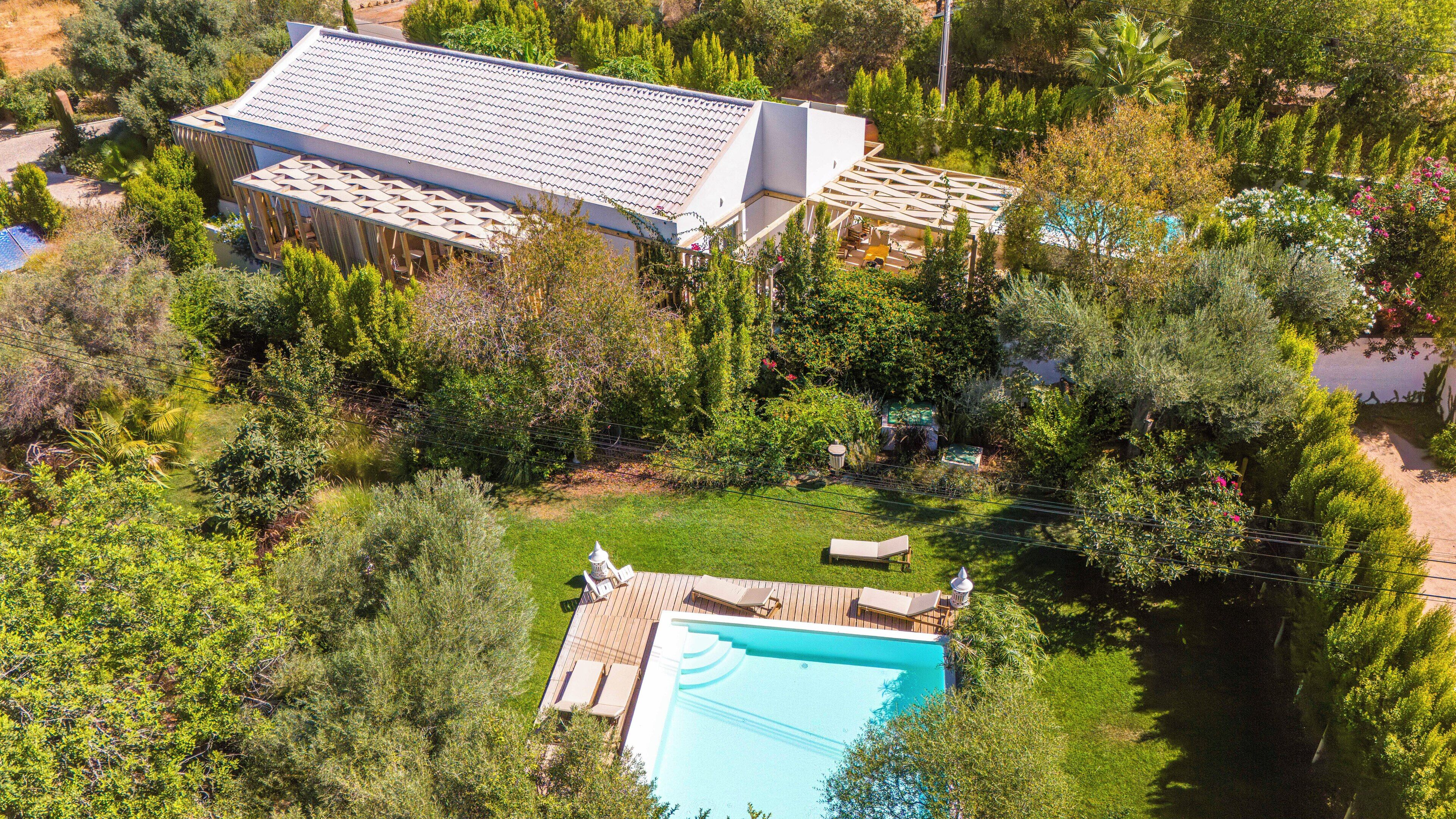 An aerial view of a property with a large building, a swimming pool, and surrounding greenery.