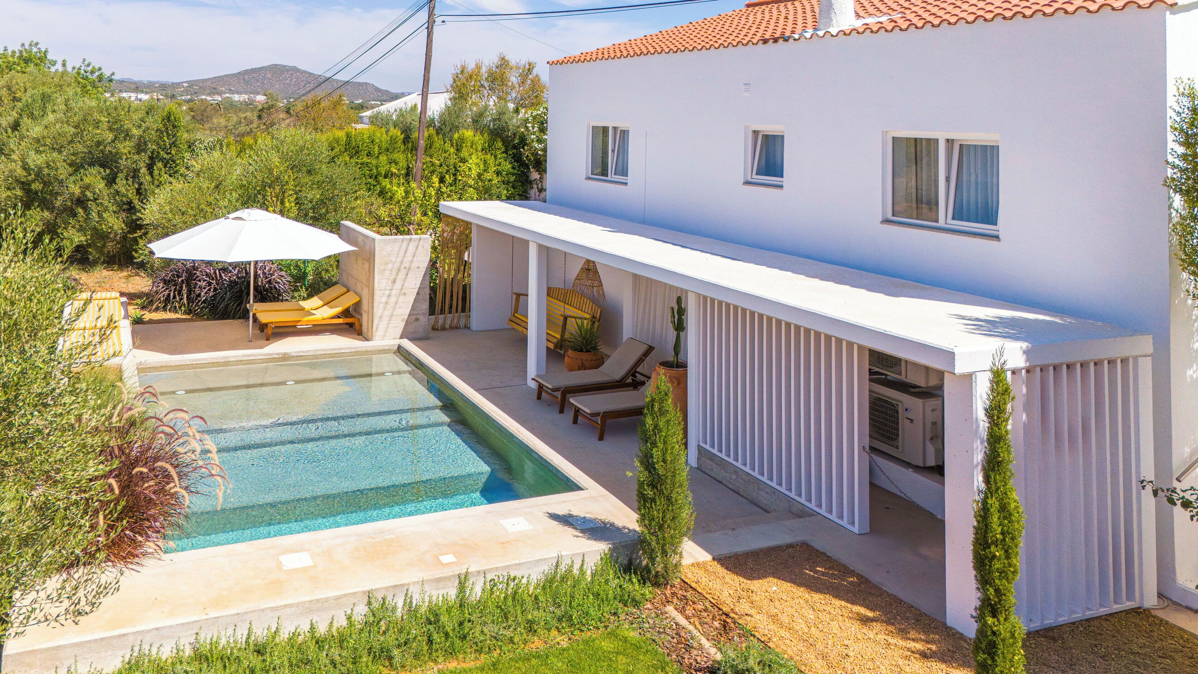 A white villa with a swimming pool, outdoor seating, and a covered patio area.