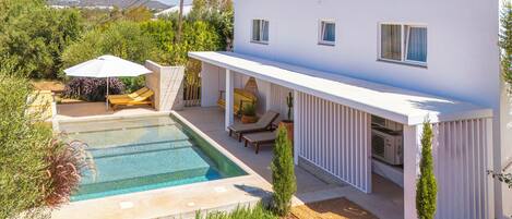 A white villa with a swimming pool, outdoor seating, and a covered patio area.