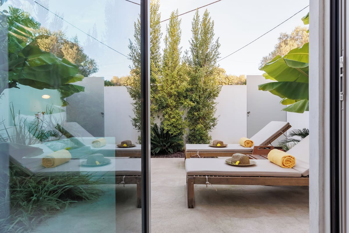 A modern outdoor lounge area with two wooden lounge chairs, each with a towel and a hat.