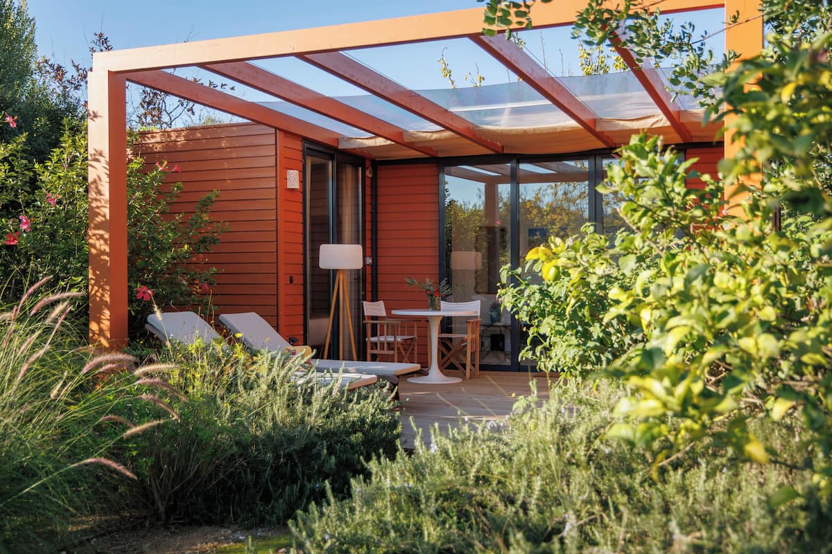 A modern outdoor seating area with a glass enclosure, wooden walls, and a small table with chairs.