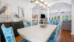 Een ruime eethoek met een grote tafel, blauwe gestreepte stoelen en een kroonluchter.