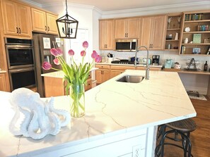 Une cuisine moderne avec des meubles en bois, des appareils en acier inoxydable, un plan de travail en marbre et un vase de tulipes.
