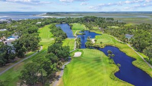 Een golfbaan met diverse waterhindernissen, omgeven door weelderige begroeiing en woonhuizen.