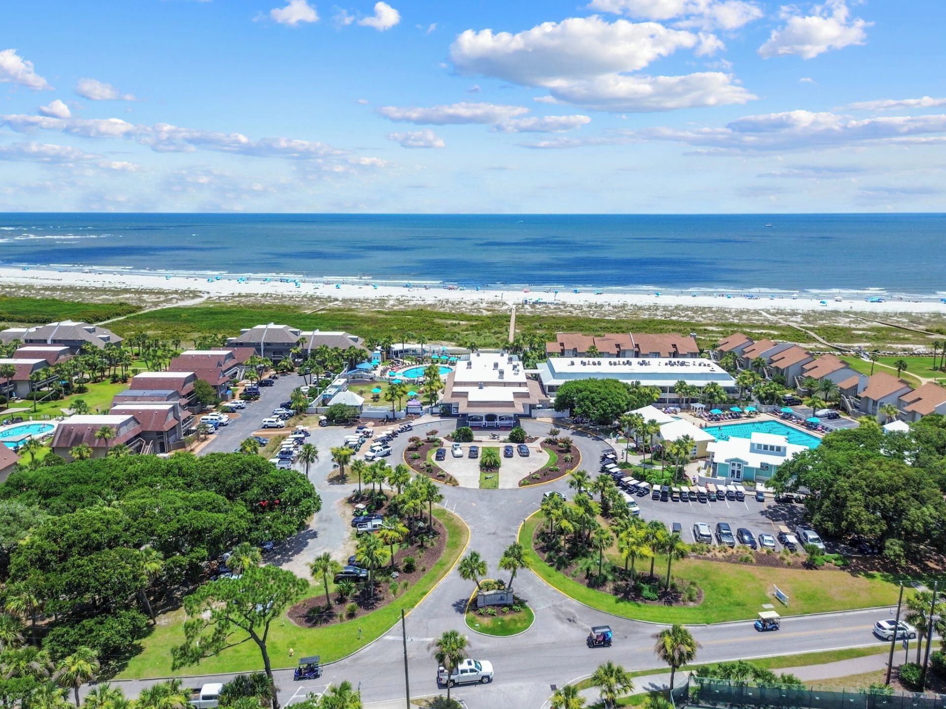 Een resort met meerdere gebouwen, een zwembad in het centrum en uitzicht op het strand.