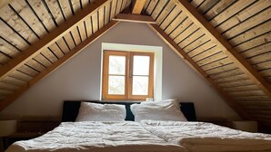 Un dormitorio con techo de madera inclinado, una ventana y una cama con ropa blanca.