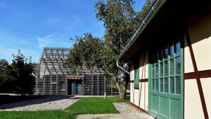 Un edificio moderno con techo inclinado y puerta verde, rodeado de césped cuidado y árboles.