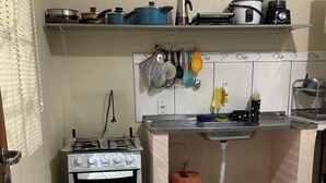 Une cuisine de taille réduite, équipée d’une cuisinière à gaz, d’un four et d’un évier placé sous un plan de travail.