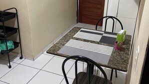 Un petit coin repas avec une table et deux chaises, une porte en bois, un porte-clés fixé au mur et une étagère en métal.
