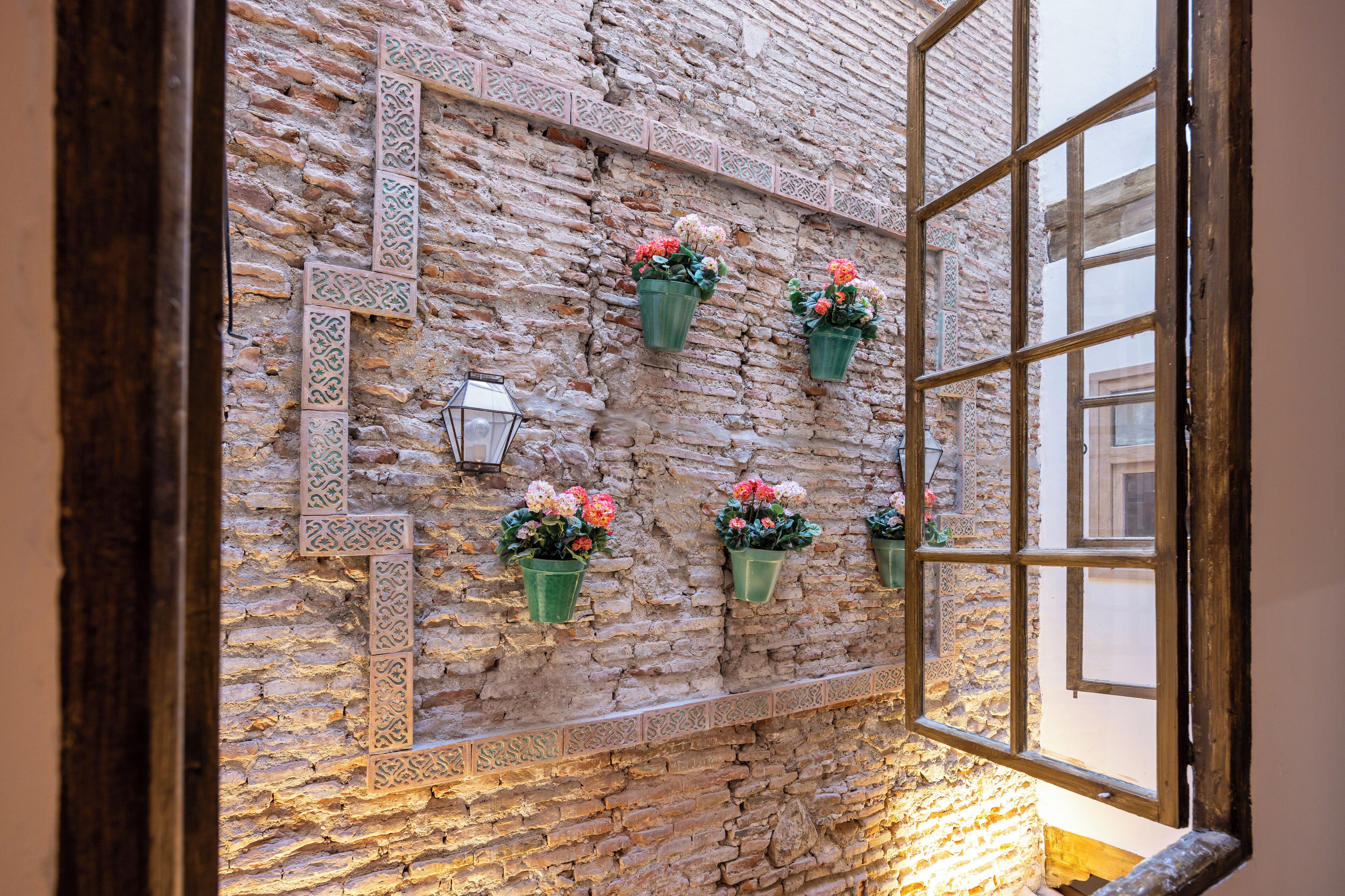 Une pièce avec un mur en pierre, une fenêtre et des jardinières décoratives suspendues, ornées de fleurs.