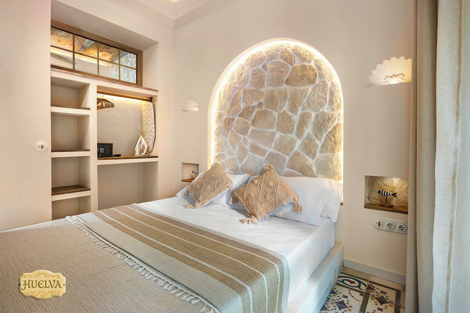 Un dormitorio con cabecera de piedra, cama con ropa de cama a rayas y estantería empotrada.