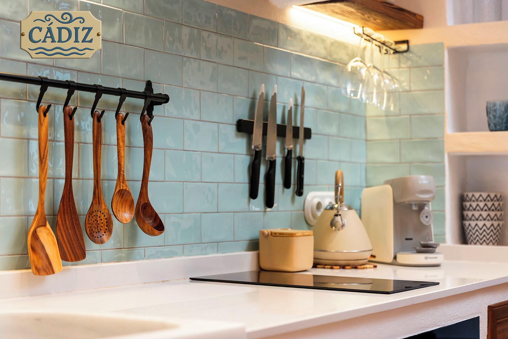 Una cocina con utensilios de madera colgados en un perchero, una cafetera y un tostador sobre la encimera.