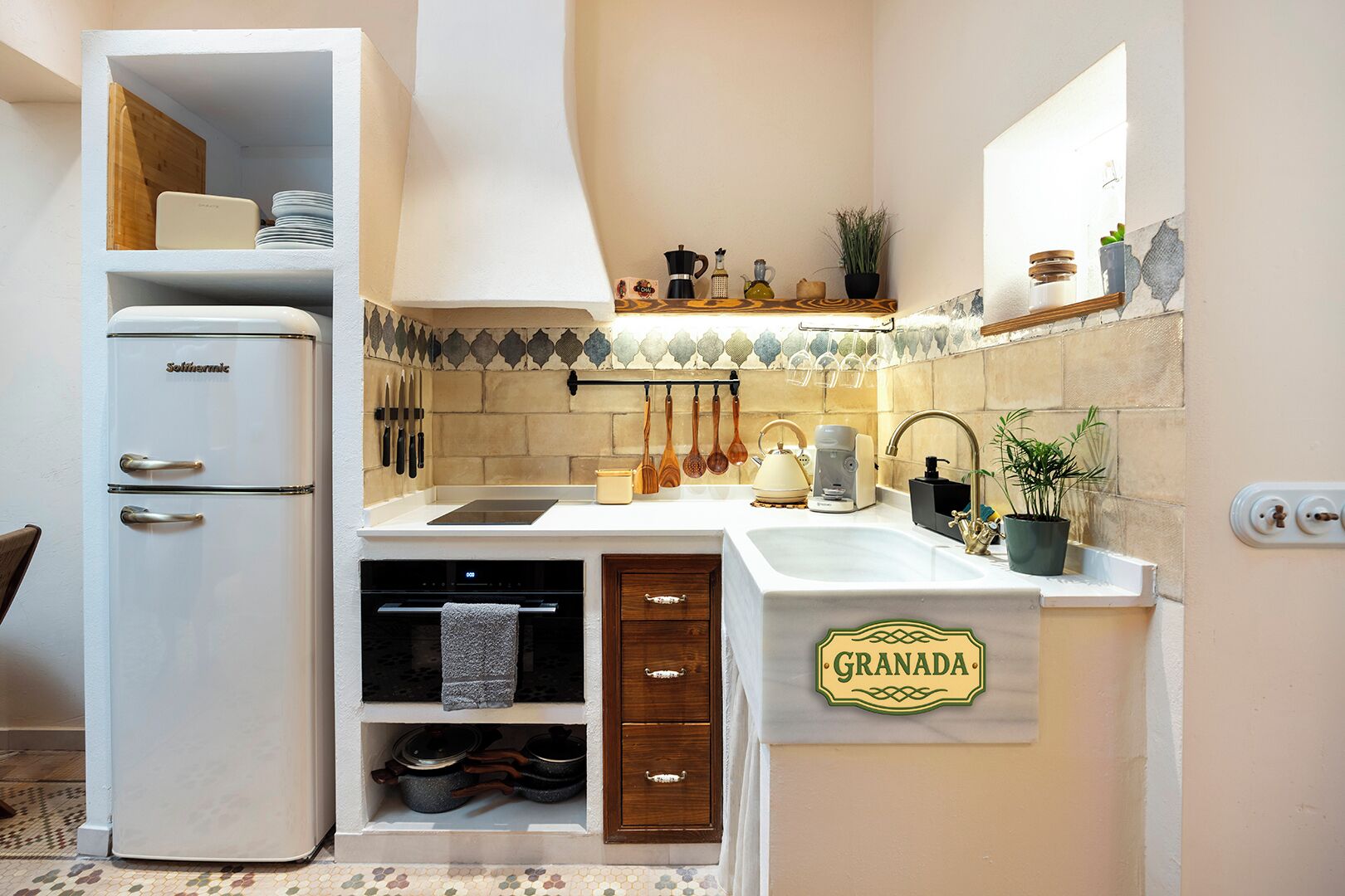 Een kleine keuken met een witte koelkast, een spoelbak en een aanrecht met een 'GRANADA' bordje.