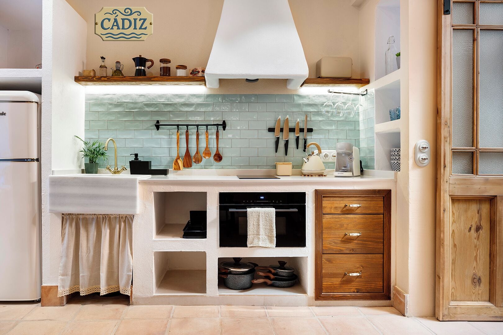 A kitchen with a tiled backsplash, wooden cabinets, and a hanging utensil rack.