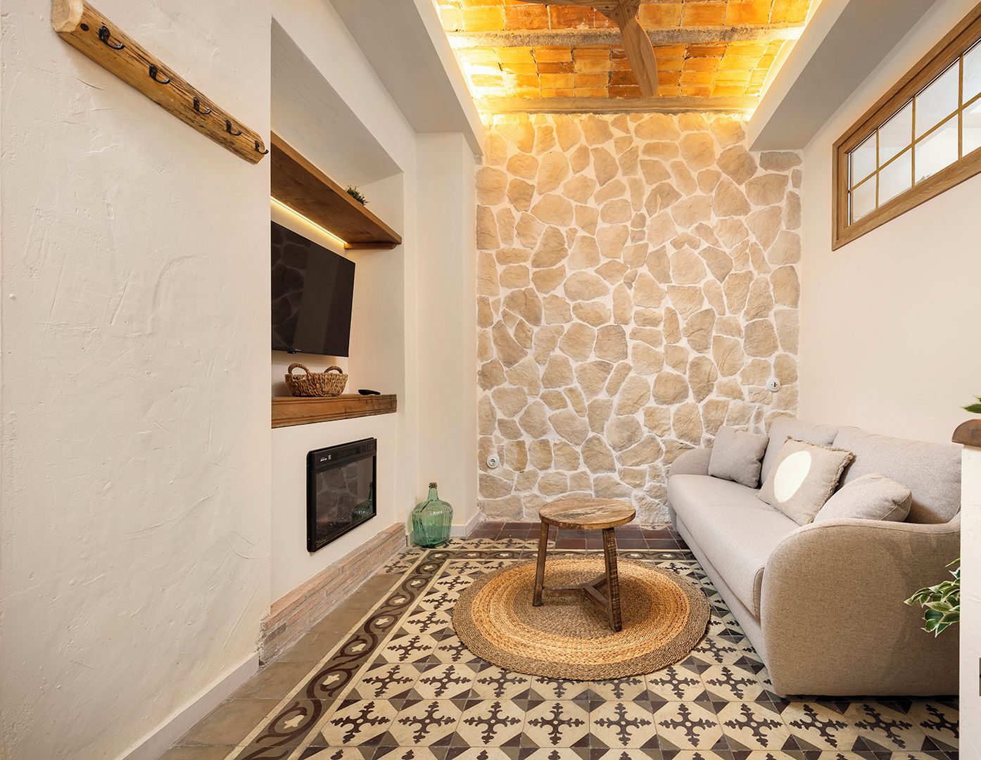 Una sala de estar acogedora con una pared de piedra, un sofá, un televisor y un suelo con diseño.