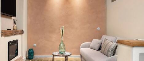 Una sala de estar con un sofá, una mesita redonda con un florero, un televisor montado en la pared y una alfombra estampada.