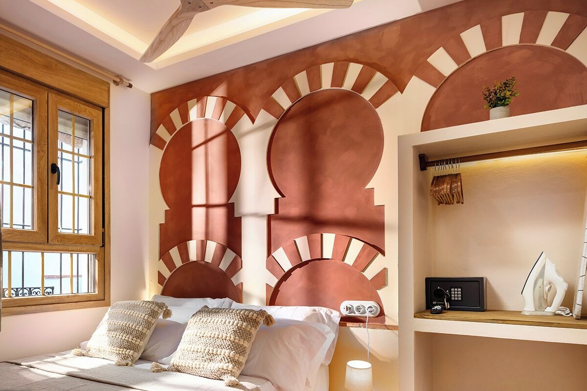 A bedroom with a bed, a nightstand, a lamp, and a shelf with an iron and a radio.