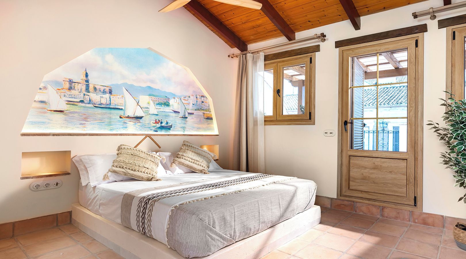 Un dormitorio con cama, un cuadro de una escena costera, una puerta de madera y suelo de baldosas.