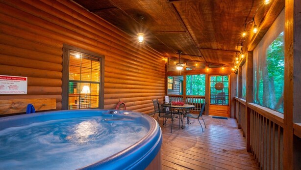 Une cabane en bois dotée d’un bain à remous, d’un coin repas et de grandes fenêtres offrant une vue sur la forêt.