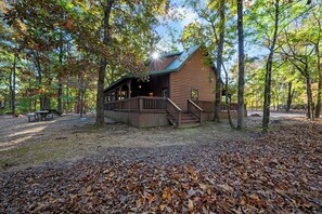A rustic cabin with a deck, surrounded by trees and a picnic area.