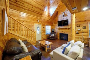 L’intérieur d’une cabane en rondins, avec une cheminée, un canapé en cuir, un plancher en bois et un téléviseur fixé au mur.