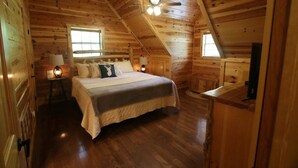Une chambre confortable dans un chalet en bois, avec un lit, des lampes de chevet et un ventilateur de plafond.