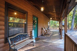 A wooden cabin with a porch, a bench, and a rocking chair.