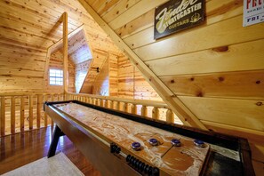 A room with a shuffleboard table, wooden walls, and a sloped ceiling.